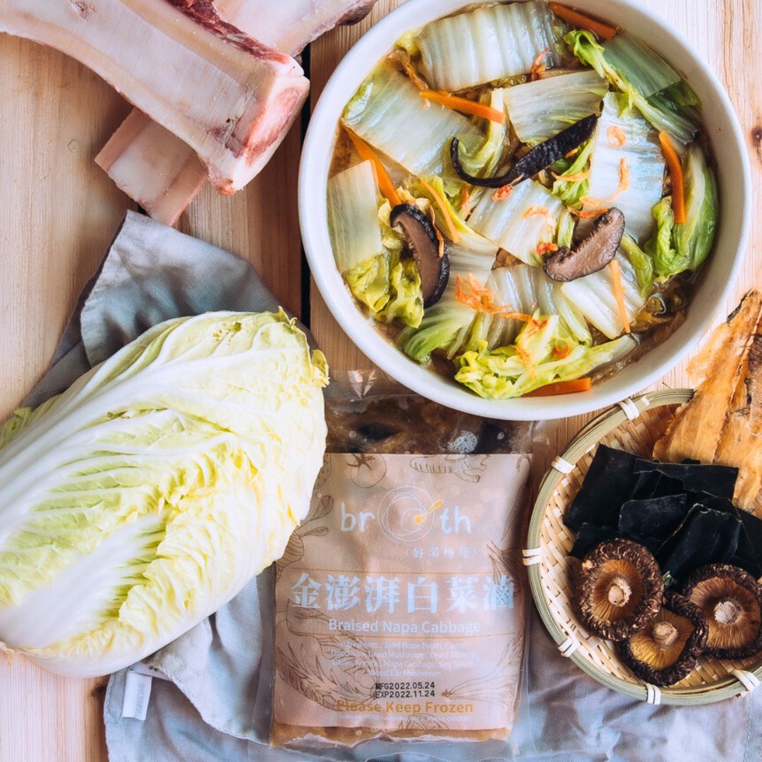 Bowl of Braised Napa Cabbage, a head of cabbage, and a package of napa cabbage on a wooden surface.