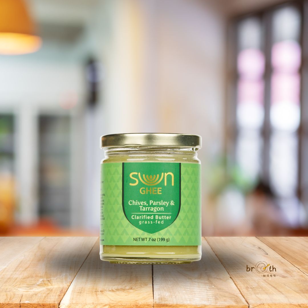 A jar of Sun Ghee Chives, Parsley & Tarragon clarified butter (7 oz) placed on a wooden surface with a softly blurred kitchen background.