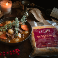 A bowl of Beef Bourguignon with beef, carrots, potatoes, and pearl onions in a red wine stew beside the frozen product package labeled “好湯慢慢 Beef Bourguignon 紅酒燉牛肉,” styled with candlelight, wine, and festive décor.