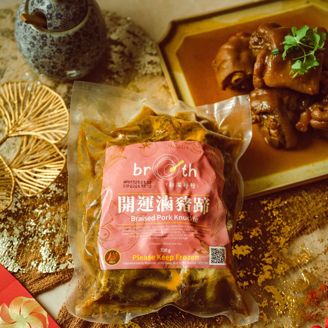 A frozen pack of Braised Pork Knuckle from Broth (好湯慢慢) placed on a festive table setting with a plated pork knuckle dish in sauce, accented with gold textures and traditional holiday elements.