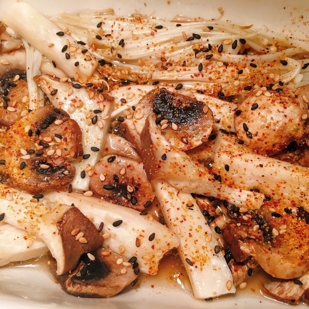 Grilled mixed mushrooms topped with Kamisharaku Yuzu Shichimi, sesame seeds, and a drizzle of sauce — a fragrant Japanese spice blend adding citrus aroma and gentle heat.