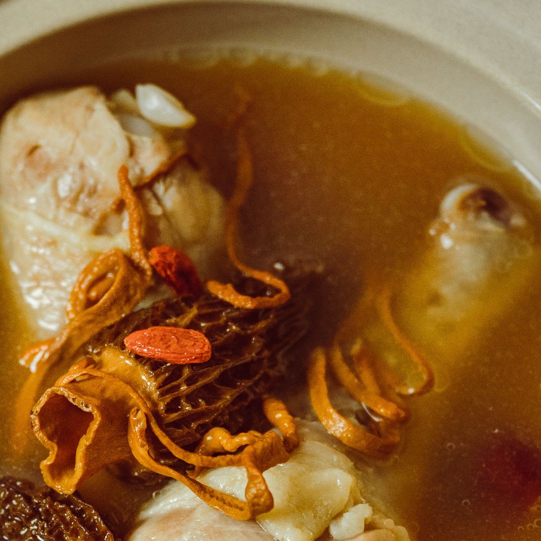 Close-up of Morel & Cordyceps Vitality Chicken Soup with chicken pieces, cordyceps, morel mushrooms, and goji berries in a clear, nourishing broth.