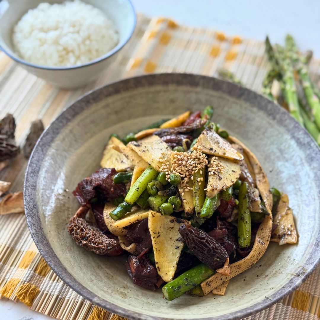 A warm, home-cooked bowl of Truffle-Infused Lightly Braised Vegetable Pot featuring asparagus, bamboo shoots, tofu skin, morel mushrooms, and cured meat slices, lightly seasoned with black truffle and sesame seeds. Served with a side of white rice for a balanced, comforting meal.