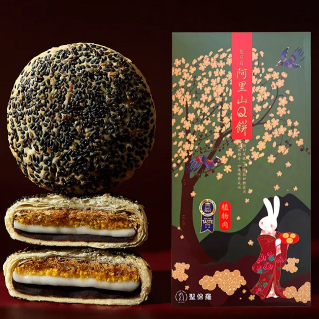 Traditional Chinese mooncake with sesame seeds on one side, sliced open to show filling, next to a decorative packaging box with cherry blossoms and a rabbit.