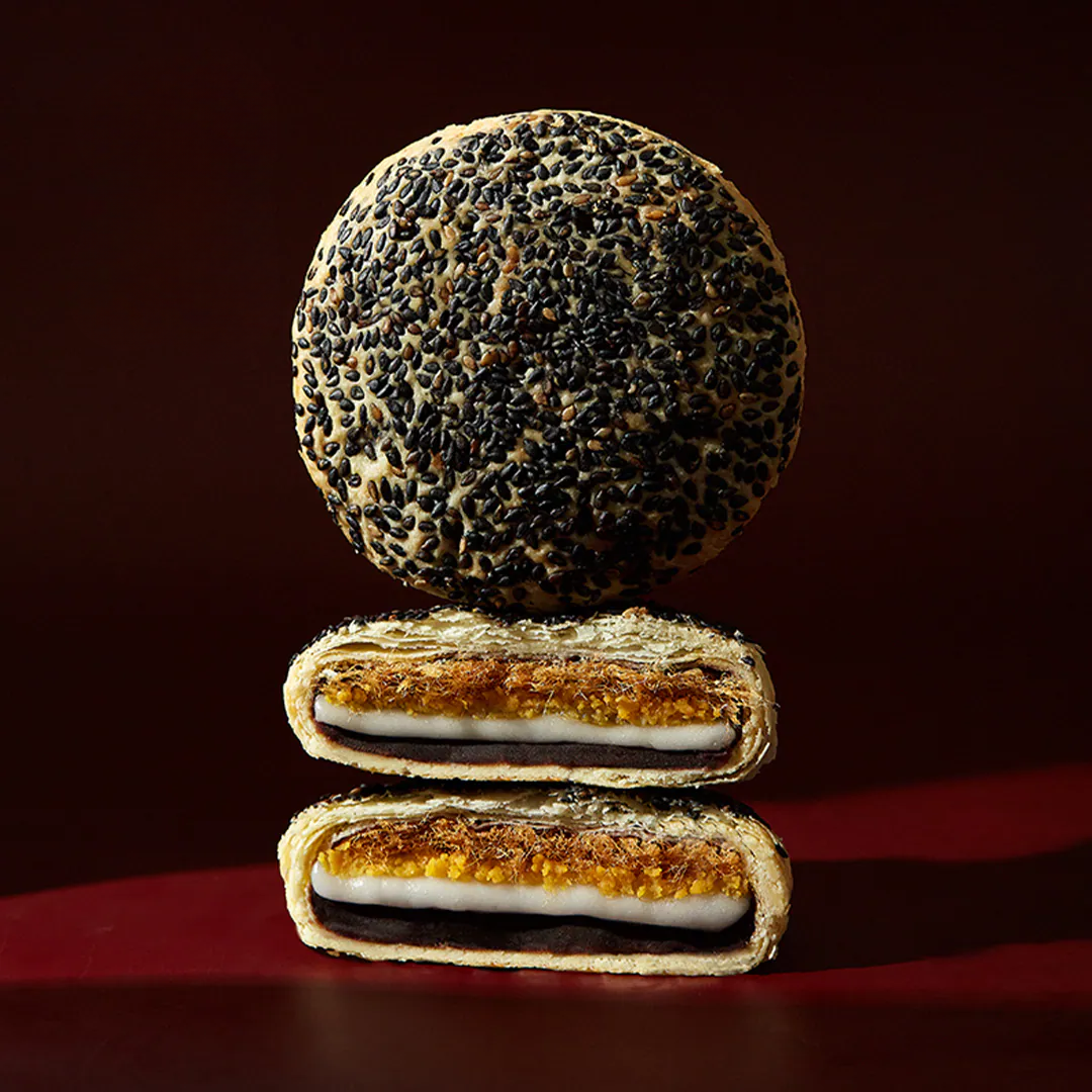 Two halves of a black sesame seed cookie stacked on a dark background