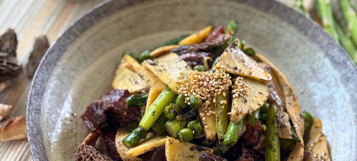 A warm, home-cooked bowl of Truffle-Infused Lightly Braised Vegetable Pot featuring asparagus, bamboo shoots, tofu skin, morel mushrooms, and cured meat slices, lightly seasoned with black truffle and sesame seeds. Served with a side of white rice for a balanced, comforting meal.