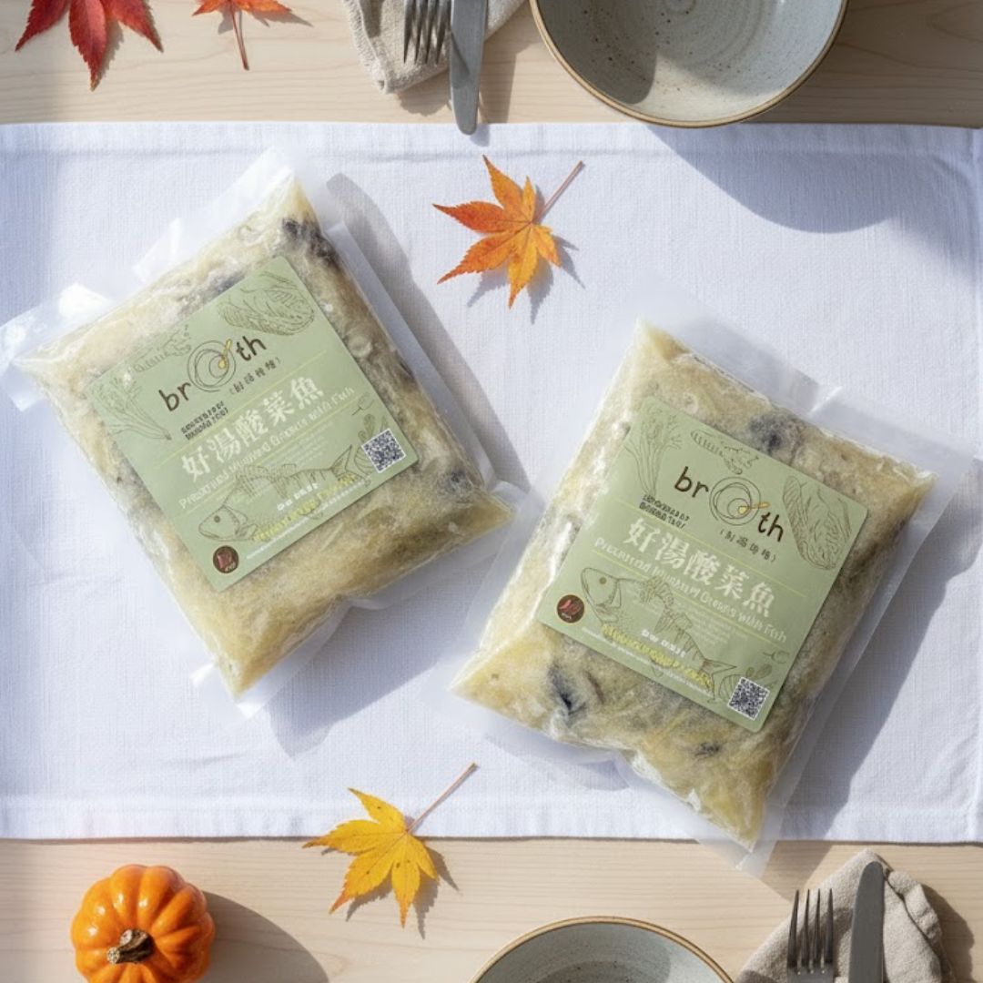 Two packs of BROTH’s Preserved Mustard Greens with Fish on a cream-toned table setting with autumn leaves, pumpkin, and tableware, creating a bright, clean Thanksgiving atmosphere.