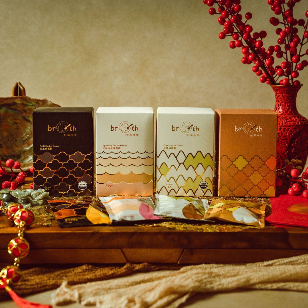 Four Broth (好湯慢慢) chicken essence gift boxes displayed side by side with sachets in front, styled on a festive table with red berries and traditional decorations.