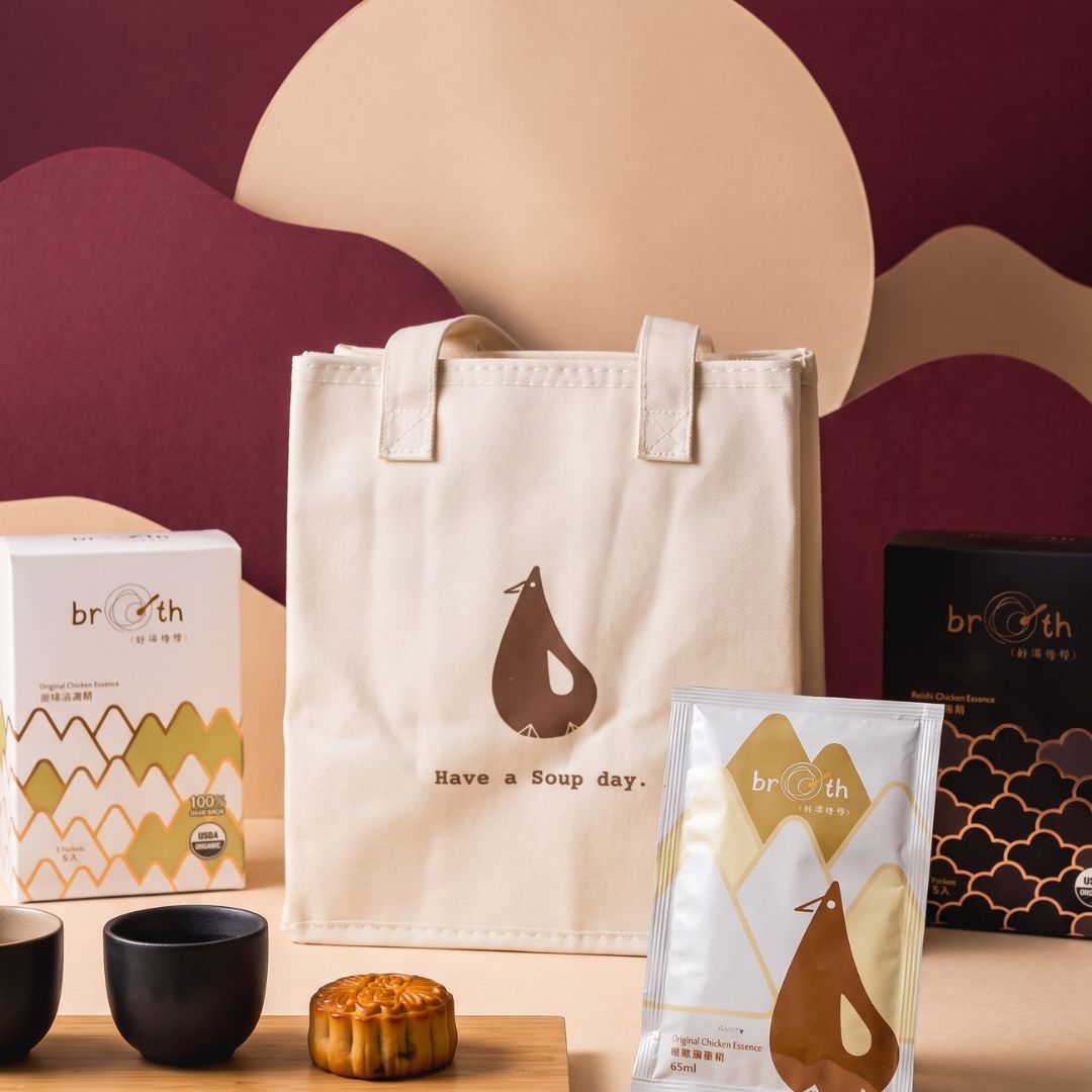 A cream canvas tote bag with a brown pear-shaped bird logo and the text 'Have a Soup day.' is displayed alongside its packaging boxes and a small mooncake on a styled tabletop.