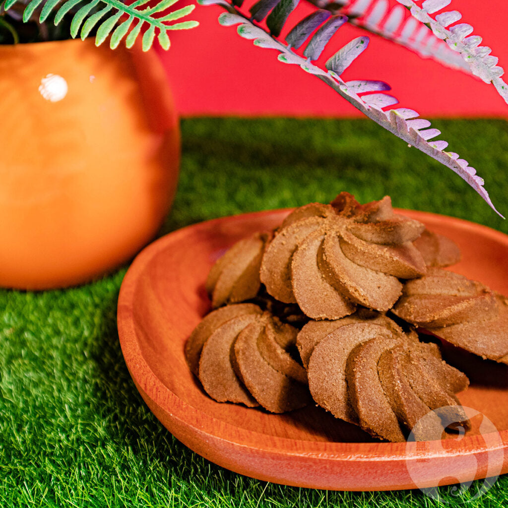 Pumpkin-shaped cookies on a wooden plate with a pumpkin and decorative leaves in the background.